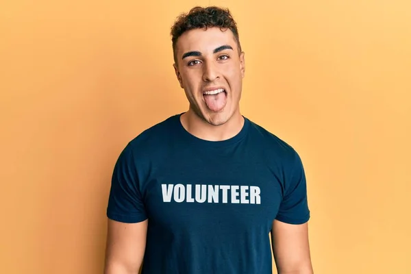 Jovem Hispânico Vestindo Camiseta Voluntária Colando Língua Feliz Com Expressão — Fotografia de Stock