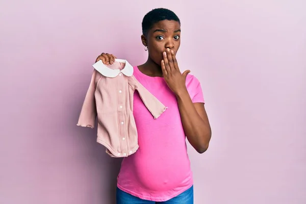 Joven Mujer Afroamericana Esperando Bebé Sosteniendo Ropa Cubriendo Boca Con — Foto de Stock