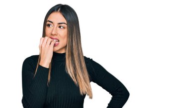 Günlük kıyafetler giyen genç İspanyol kadın gergin ve gergin görünüyor. Ağzı tırnak yiyen ellerle. anksiyete. 