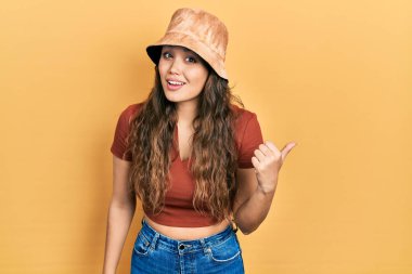 Gündelik kıyafetler giyen ve şapkalı neşeli yüzlü gülümseyen genç İspanyol kız başparmağıyla yan tarafı işaret ediyor.. 