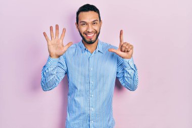 Sakallı, sıradan mavi tişörtlü İspanyol bir adam yedi numaralı parmaklarını gösterip gösterirken kendine güvenen ve mutlu bir şekilde gülümsüyor.. 