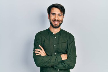 Gündelik kıyafetler giyen, kollarını kavuşturup kameraya gülümseyen genç İspanyol adam. pozitif kişi. 