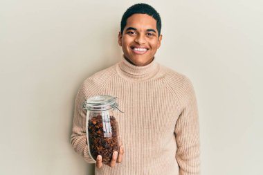 Genç, yakışıklı, elinde kuru üzümlerle dolu bir kavanoz tutan yakışıklı adam. Olumlu ve mutlu görünüyor. Kendine güvenen bir gülümsemeyle dişlerini gösteriyor. 