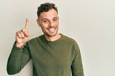 Gündelik kıyafetler giyen genç İspanyol bir numarayı gösterip işaret ederken kendinden emin ve mutlu bir şekilde gülümsüyor.. 