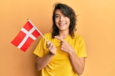 Danimarka bayrağını tutan genç İspanyol kadın mutlu bir şekilde el ve parmağıyla işaret ediyor. 