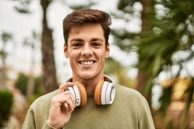 Şehirde kulaklık takarak mutlu gülümseyen genç İspanyol adam..