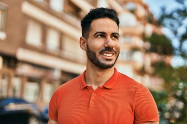 Genç İspanyol adam gülümseyerek şehirde mutlu mesut dikiliyor..