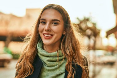 Genç sarışın kız gülümsüyor, mutlu bir şekilde şehirde duruyor..