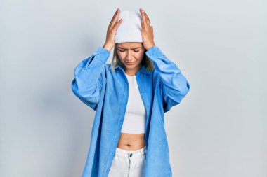 Güzel sarışın kadın yün şapka takıyor. Baş ağrısı çekiyor. Acı ve migren yüzünden çaresiz ve stresli. Eller başının üstünde.. 