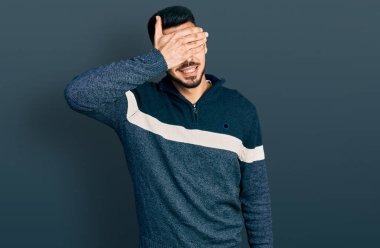 Sakallı, sıradan bir kazak giyen, gülümseyen ve yüzünde şaşkınlıktan gözleri kapayan genç İspanyol bir adam. kör kavram. 