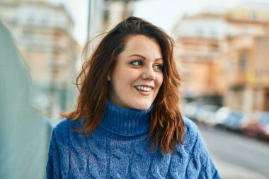 Genç İrlandalı artı cüsseli kız gülümseyerek şehirde mutlu mesut duruyor..