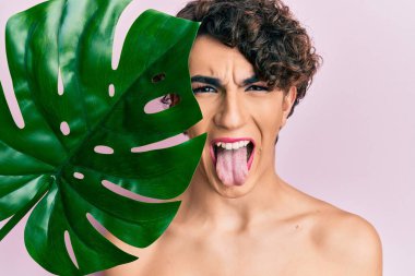 Genç adam yeşil bitki yaprağı tutarak makyaj yapıyor. Güzel bir yüze yakın. Dilini dışarı çıkarıyor.. 