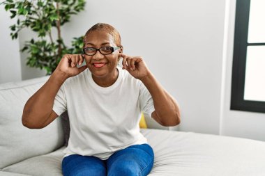 Evde koltukta oturan olgun İspanyol kadın yüksek sesli müzik sesi için kulaklarını parmaklarıyla kapatıyor. sağır kavramı. 