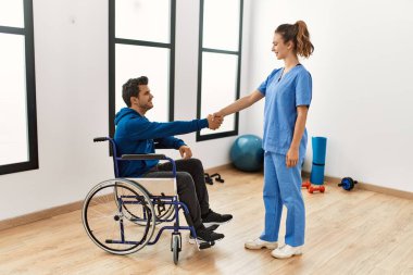 Genç engelli adam ve fizyoterapist klinikte mutlu bir şekilde el sıkışıyor..