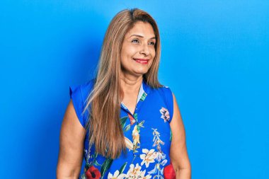 Orta yaşlı İspanyol kadın gündelik kıyafetler giyip yüzünde gülümsemeyle yan yana bakıyor, doğal bir ifade. Kendinden emin gülen. 