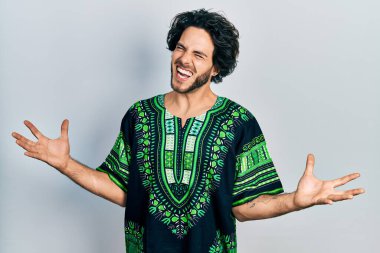 Geleneksel Afrika kıyafetleri giyen yakışıklı İspanyol adam. Deli gibi bağırıyor, bağırıyor, agresif bir ifade ve kollarla bağırıyor. hüsran kavramı. 