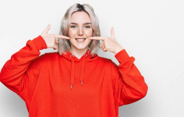 Sıradan kıyafetler giyen, neşeli gülümseyen, parmaklarıyla ve ağzıyla işaret eden genç sarışın kız. diş sağlığı kavramı. 