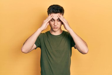 Kulakları genişlemiş, günlük yeşil tişörtler giyen, baş ağrısı çeken, çaresiz ve stresli genç beyaz bir çocuk. Çünkü acı ve migren. Eller başının üstünde.. 