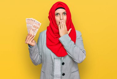İslami tesettür takan güzel İspanyol kadın elinde Türk lirası banknotlarla ağzını eliyle kapatıyor, şok geçiriyor ve hata yapmaktan korkuyor. şaşırmış ifade 