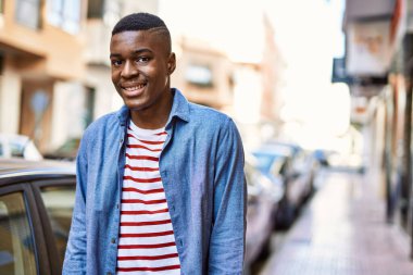 Genç Afrikalı Amerikalı adam gülümseyerek şehirde mutlu mesut duruyor..