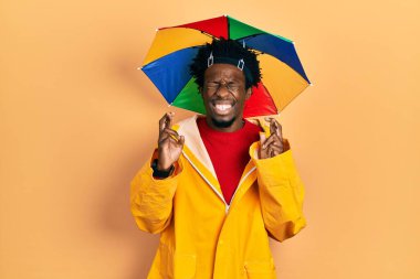 Sarı yağmurluk giyen Afro-Amerikalı genç adam umut ve gözleri kapalı gülümseyerek işaret ediyor. Şans ve batıl inançlar. 