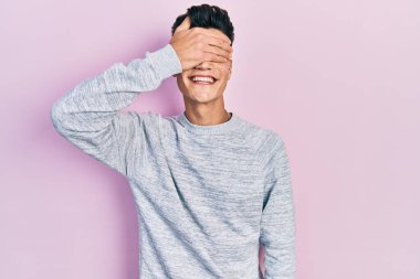 Gündelik kıyafetler giyen, gülümseyen ve gülümseyen genç İspanyol adam şaşırmak için gözlerini kapatıyor. kör kavram. 