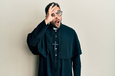 Beyaz arka plan üzerinde duran İspanyol üniformalı genç adam şaşırmış yüz ifadesiyle şaşırmış, parmaklarının arasından bakan bir jest yapıyor. İnançsız ifade. 