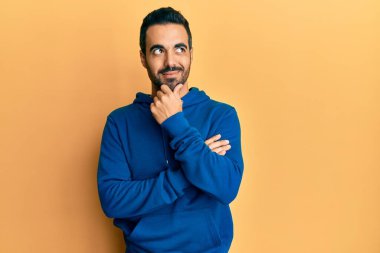 Elleri çenesinde gündelik giysiler içinde soru soran genç İspanyol bir adam, düşünceli bir ifade. Düşünceli bir yüzle gülümsüyor. şüphe kavramı. 