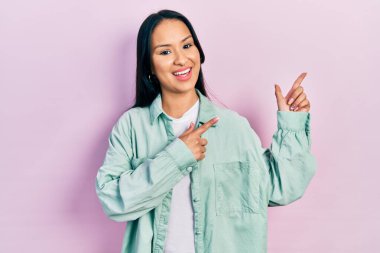 Güzel İspanyol kadın, burun piercingli, sıradan yeşil ceketli, gülümseyen ve kameraya bakan, iki eli ve parmakları yanda olan.. 