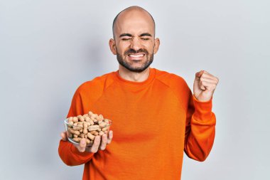 Fıstık tutan genç kel adam gururla bağırıyor, zaferi kutluyor ve başarıyı kollarını kaldırarak kutluyor. 