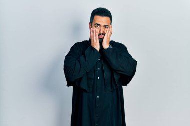 Sakallı yakışıklı, Katolik rahip cübbesi giyen, yüzü, depresyonu ve üzüntüyü örten, sıkıntılı ve tedirgin bir adam. 