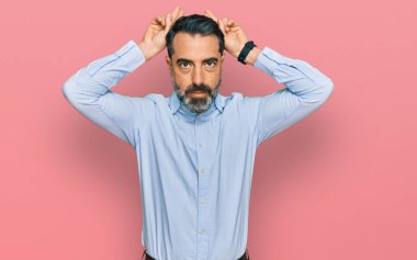 Orta yaşlı, sakallı, iş gömleği giyen, tavşan kulağı yapan, avuçlarıyla alaycı ve şüpheci görünen bir adam. Paskalya tavşanı konsepti. 