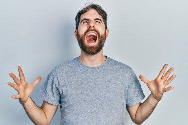 Gri bir tişört giyen, beyaz sakallı çılgın ve sinirli bir adam agresif bir ifadeyle bağırıyor ve kollarını kaldırıyor. hüsran kavramı. 