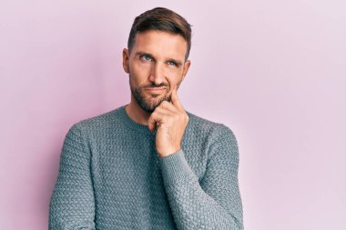 Sakallı, sıradan bir süveter giyen yakışıklı bir adam şüpheye odaklanmış, çenesinde parmak olan ve kafasını kaldırıp merak eden biri. 