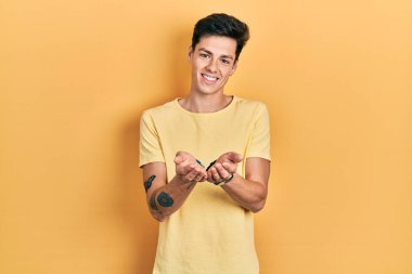 Elleri avuçlarında gülümseyen, günlük sarı tişörtler giyen İspanyol genç adam jest yapıyor. Bekleme ve koruma 