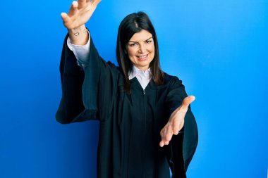 Genç İspanyol kadın yargıç üniforması giyiyor kameraya bakıyor sarılmak için kollarını açmış gülümsüyor. Mutluluğu kucaklayan neşeli bir ifade.. 