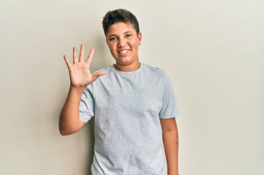 Gündelik gri tişört giyen genç İspanyol çocuk beş numarayı gösterip işaret ederken kendinden emin ve mutlu gülümsüyor.. 