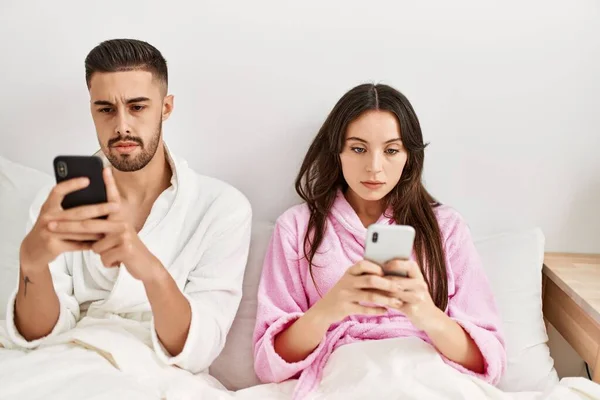 Yatakta Uzanmış Akıllı Telefon Kullanan Ciddi Yüzlü Genç Spanyol Çift — Stok fotoğraf