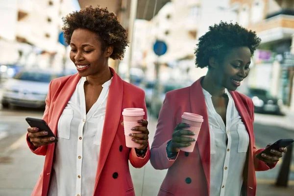 Beautiful business african american woman with afro hair smiling happy and confident outdoors at the city using smarpthone