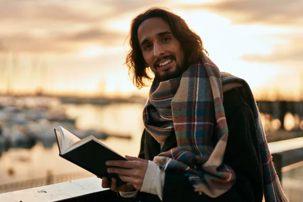 Joven Hispano Sonriendo Feliz Libro Lectura Puerto —  Fotos de Stock