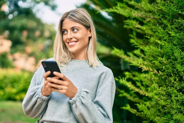 若いですブロンド女の子笑顔幸せな使用スマートフォンでザ公園 — ストック写真