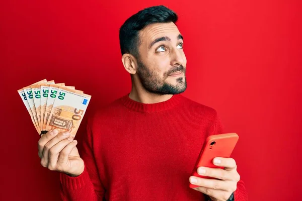 Fiatal Spanyol Férfi Okostelefont Használ Eurós Bankjegyekkel Kezében Oldalt Mosolyog — Stock Fotó
