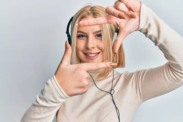 若いブロンドの女性は 幸せな顔をした手と指でフレームを作り ヘッドフォンを使用して音楽を聴いています 創造性と写真の概念 — ストック写真