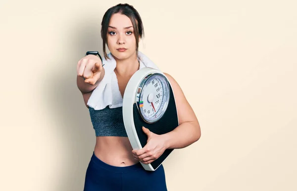 Young Hispanic Girl Wearing Sportswear Holding Weighing Machine Pointing Finger — Stock Photo, Image