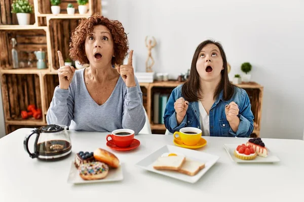 母亲和下行综合症的家庭女儿坐在家里吃早餐 惊讶地抬起头 用手指和胳膊指指着 — 图库照片