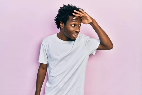 カジュアルな白いTシャツを着た若いアフリカ系アメリカ人の男性は 頭の上に手で遠くを見て非常に幸せと笑顔 検索の概念 — ストック写真