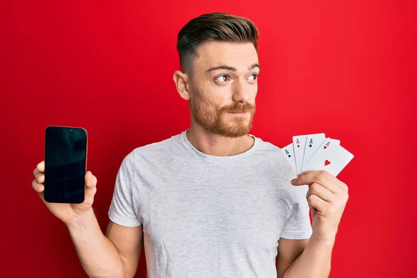 Jovem Ruivo Segurando Smartphone Cartão Casino Sorrindo Olhando Para Lado — Fotografia de Stock