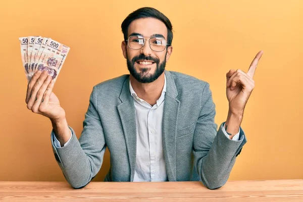 Mladý Hispánec Drží Mexické Pesos Sedí Stole Šťastně Usmívá Ukazuje — Stock fotografie