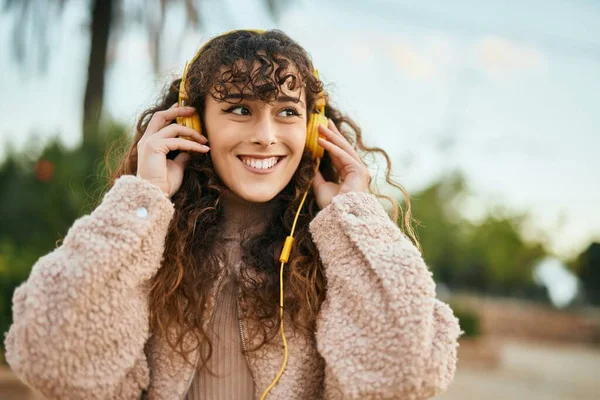 Young hispanic woman smiling happy using headphones at the city