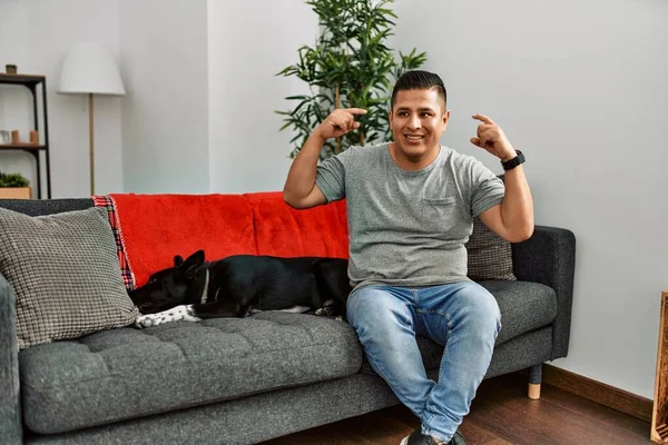 Jovem Latino Homem Cão Sentado Sofá Casa Sorrindo Apontando Para — Fotografia de Stock